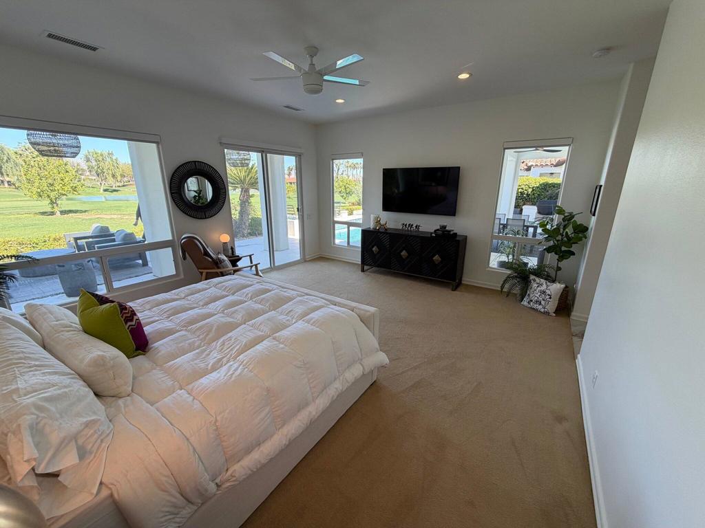 Furnished bedroom with a white bed, TV, and windows overlooking a green golf course.