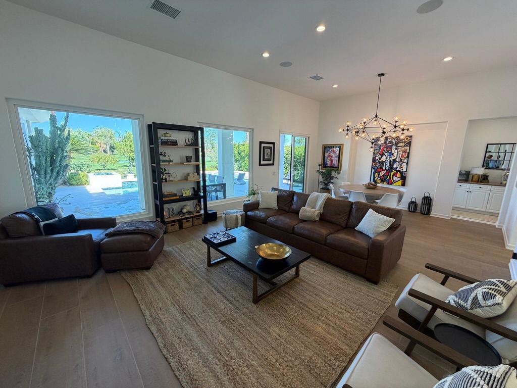 Furnished living room with brown leather sofas and large windows overlooking a pool and landscaped yard.