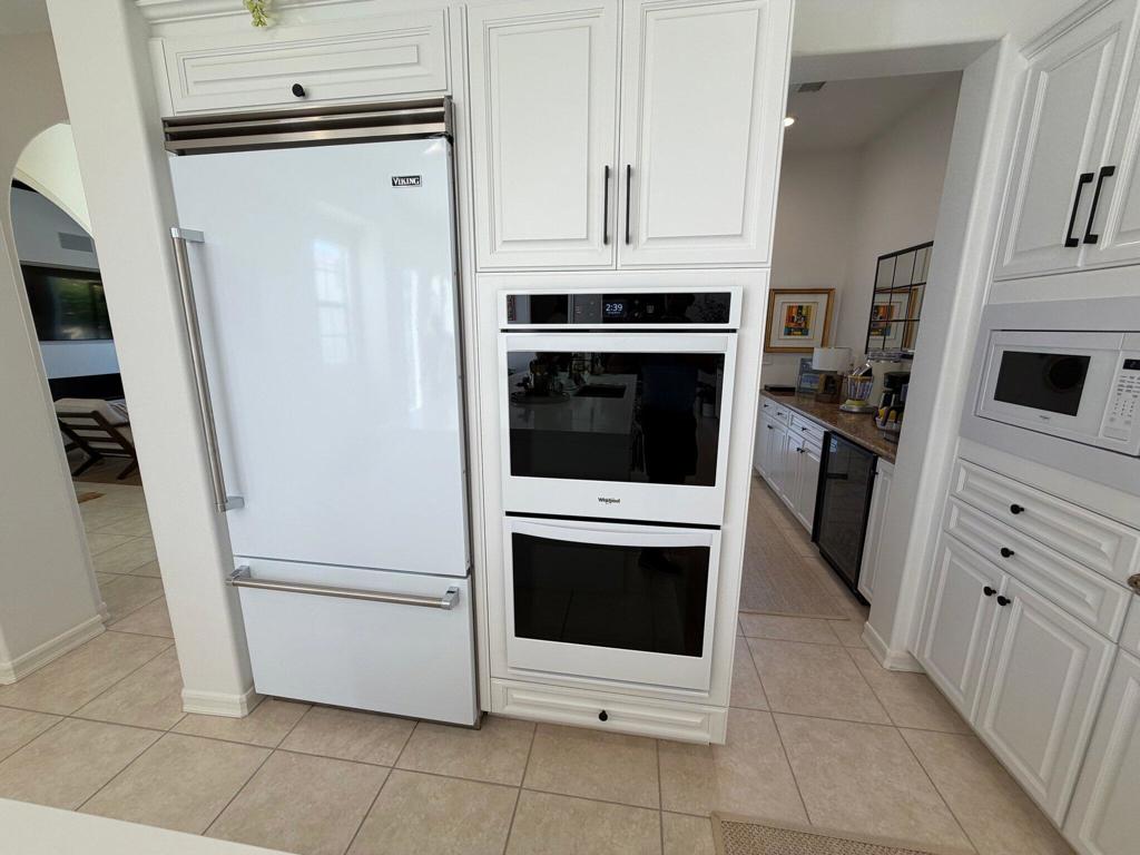 Kitchen with white cabinetry, a Viking refrigerator, and built-in double ovens.