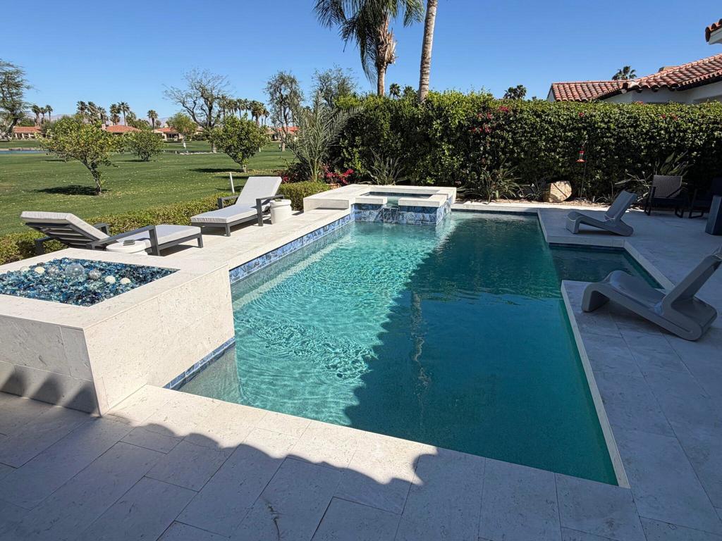 Backyard pool with raised spa, tiled deck, lounge chairs, and a broad green lawn beyond.