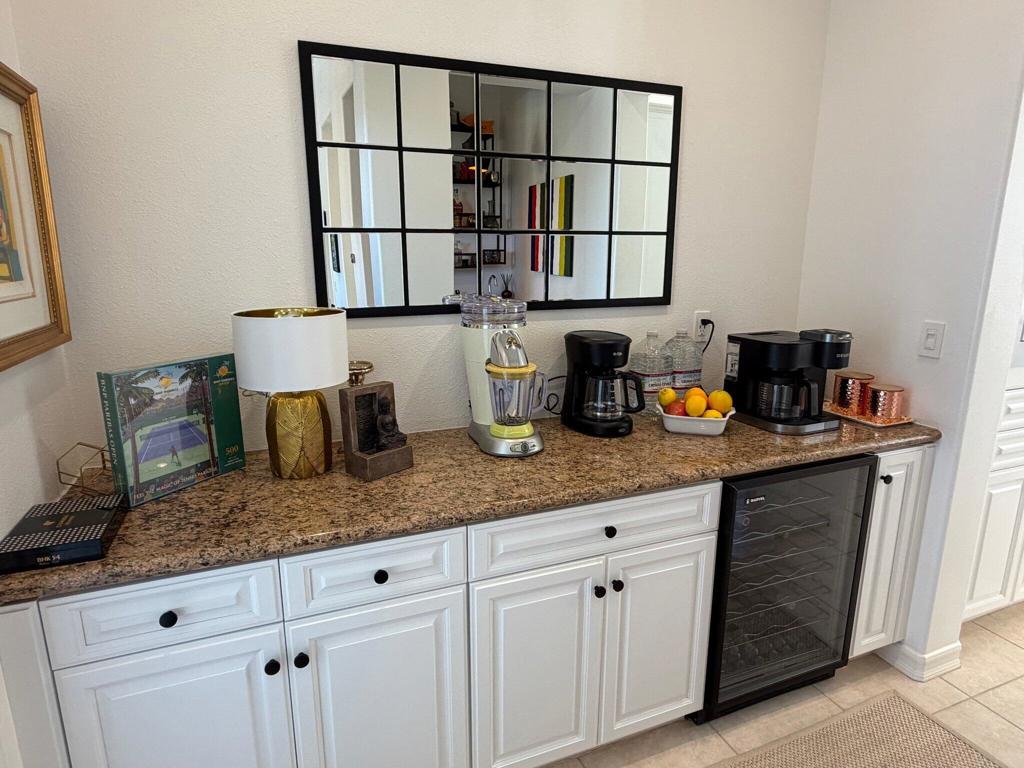 Coffee bar with a stone countertop, white cabinetry, coffee makers, and a glass-front beverage fridge.