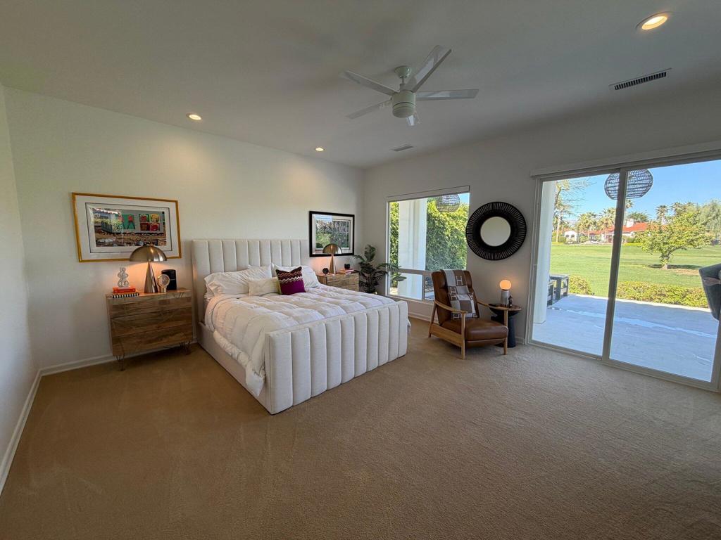 Staged bedroom with a tufted bed, lounge chair, and sliding doors overlooking a green lawn.