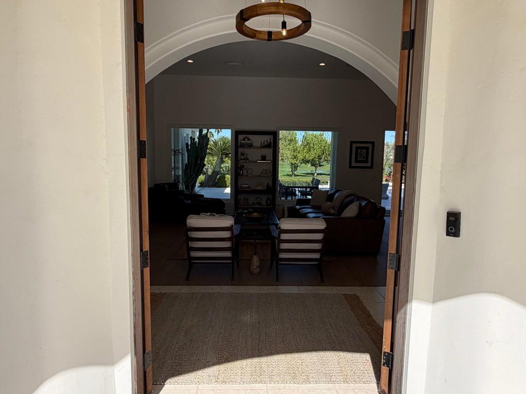 Furnished living room seen through open entry doors, with an arched ceiling and windows overlooking a green lawn.