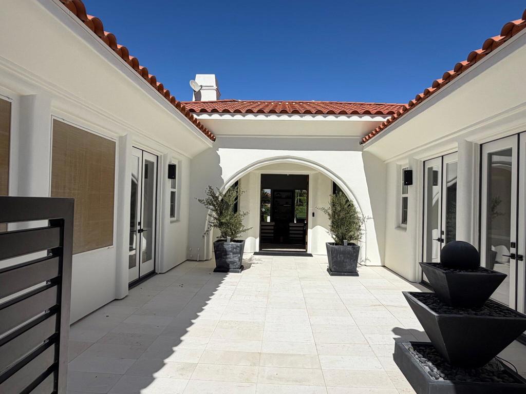 White stucco home entrance with an arched doorway, tiled courtyard, and tiered fountain.