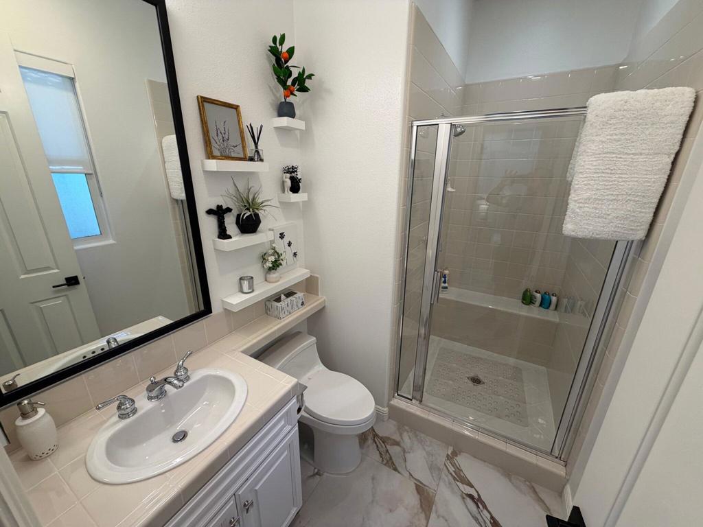 Bathroom with a glass-enclosed shower, white vanity, and decorative wall shelves.