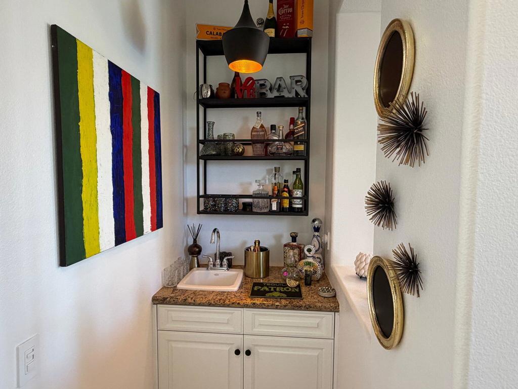 Wet bar with a granite countertop, stocked shelves, colorful artwork, and decorative mirrors.