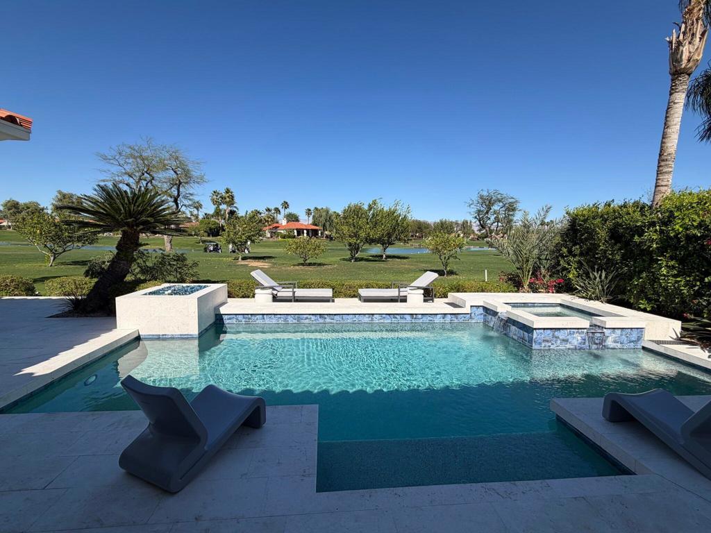 Backyard pool and spa overlooking a green golf course, with lounge chairs on the patio.