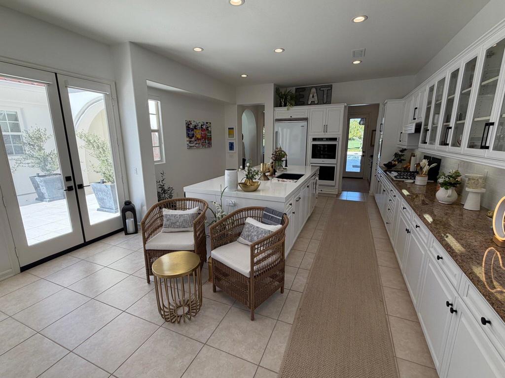 Bright white kitchen with a large island, glass-front cabinets, and patio doors.