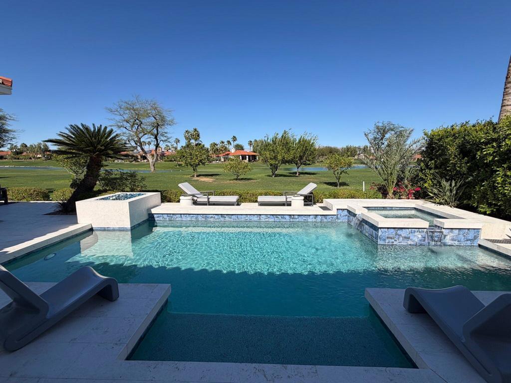Backyard pool with raised spa, lounge chairs, and a golf course and pond beyond.