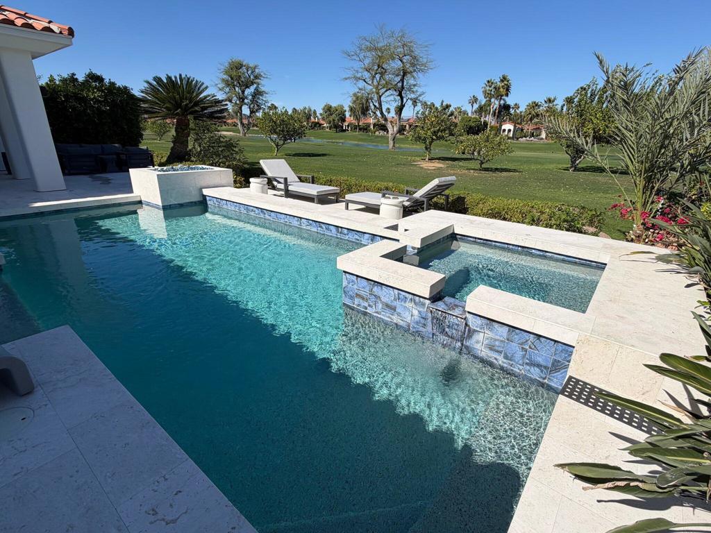 Backyard pool with raised spa, pale stone coping, and golf-course landscaping.