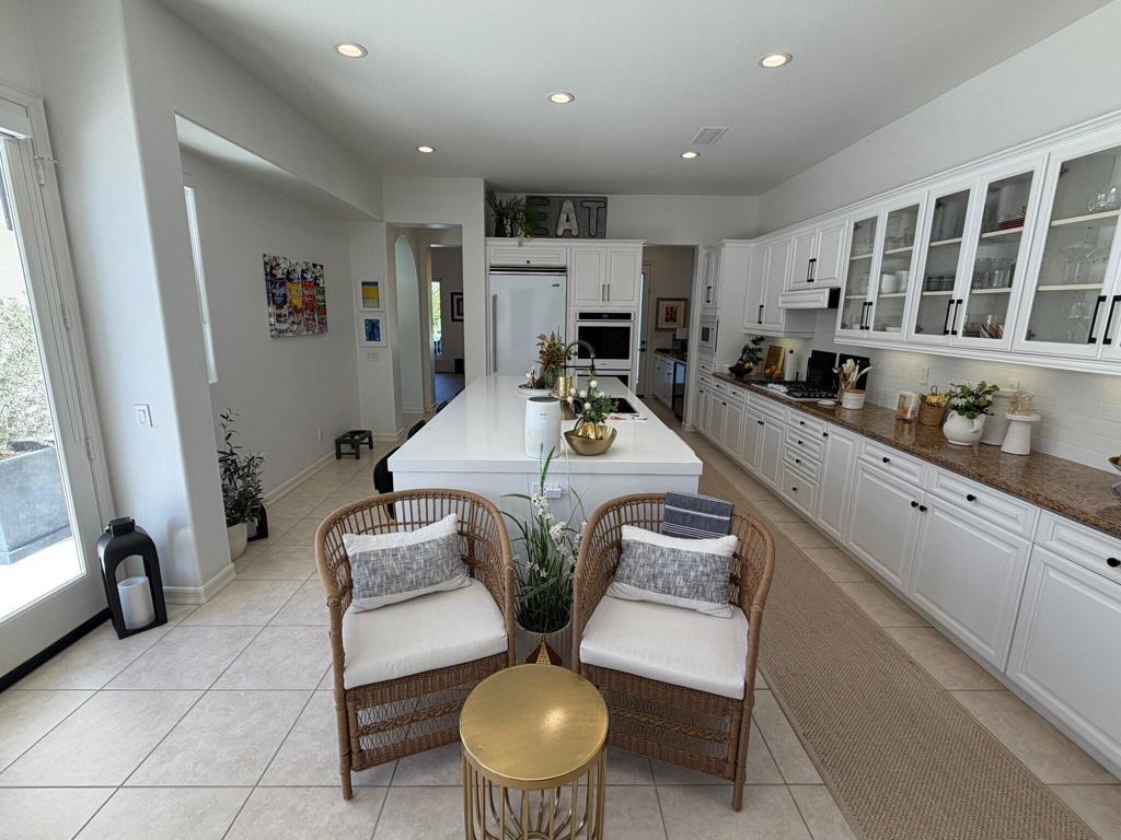 Bright white kitchen with a long island, glass-front cabinets, and wicker breakfast seating.