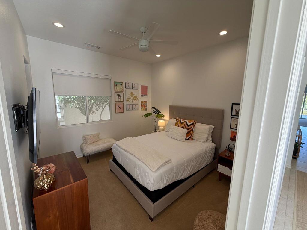 Staged bedroom with a white bed, upholstered headboard, window, and wall-mounted television.