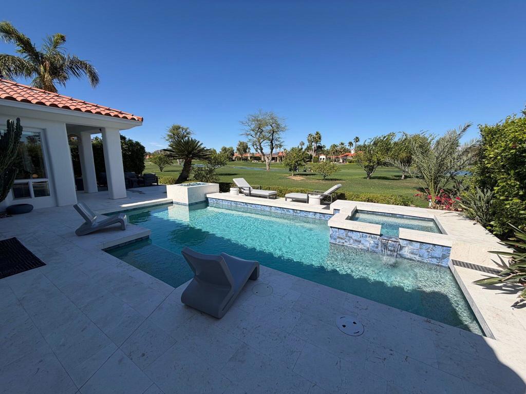 Backyard pool and spa overlooking a golf course, with lounge chairs and a tiled patio.