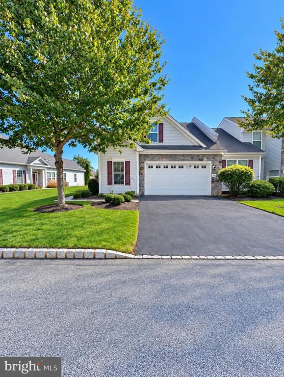 Two-story home with stone facade, attached garage, paved driveway, and mature front lawn.