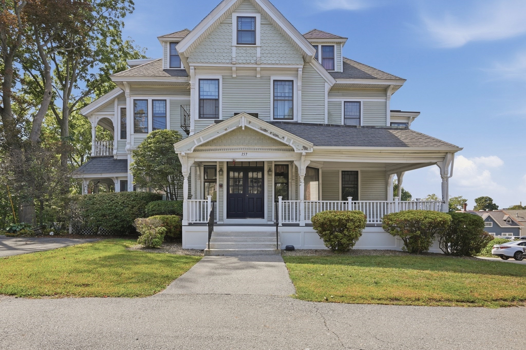 Multi-story gabled house with a broad covered porch, landscaped lawn, and walkway to the entrance.