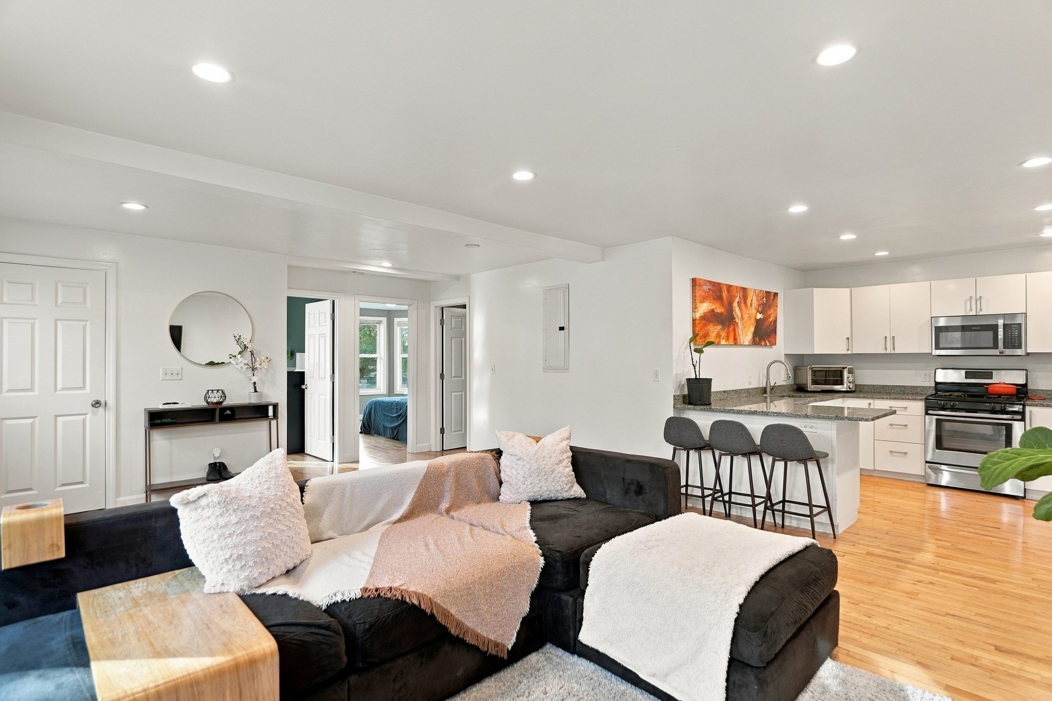 Open-plan living room and kitchen with a dark sectional sofa, breakfast bar, and hardwood floors.