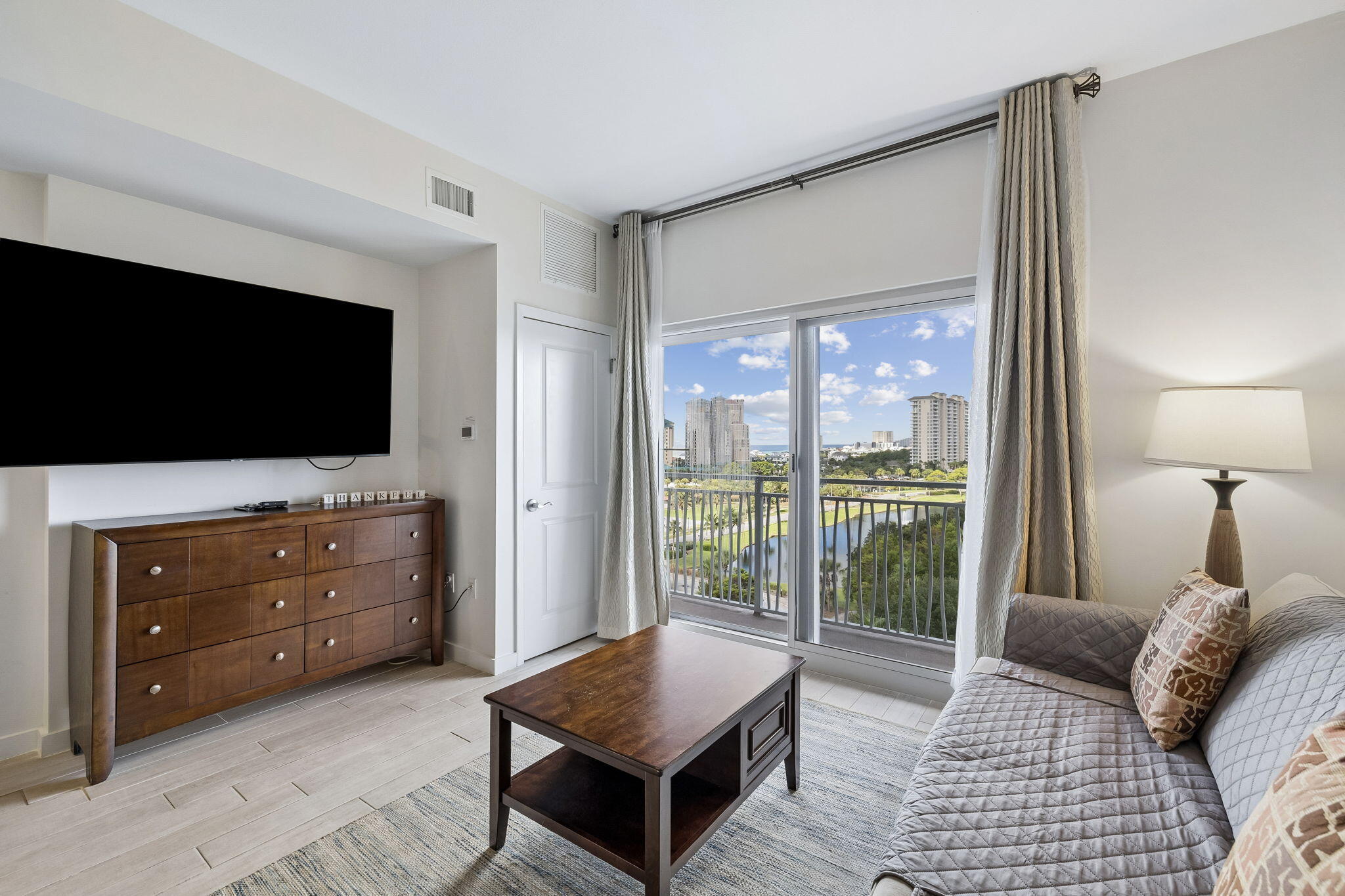 Condo living room with a gray sofa and balcony views of water and high-rises.
