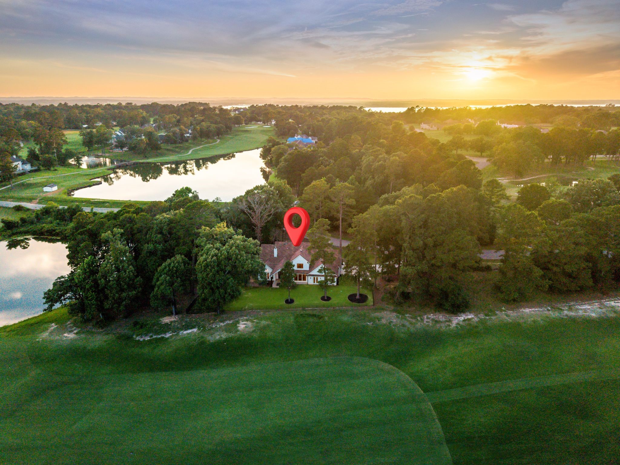 Aerial view of a house beside golf course greens and ponds at sunset.