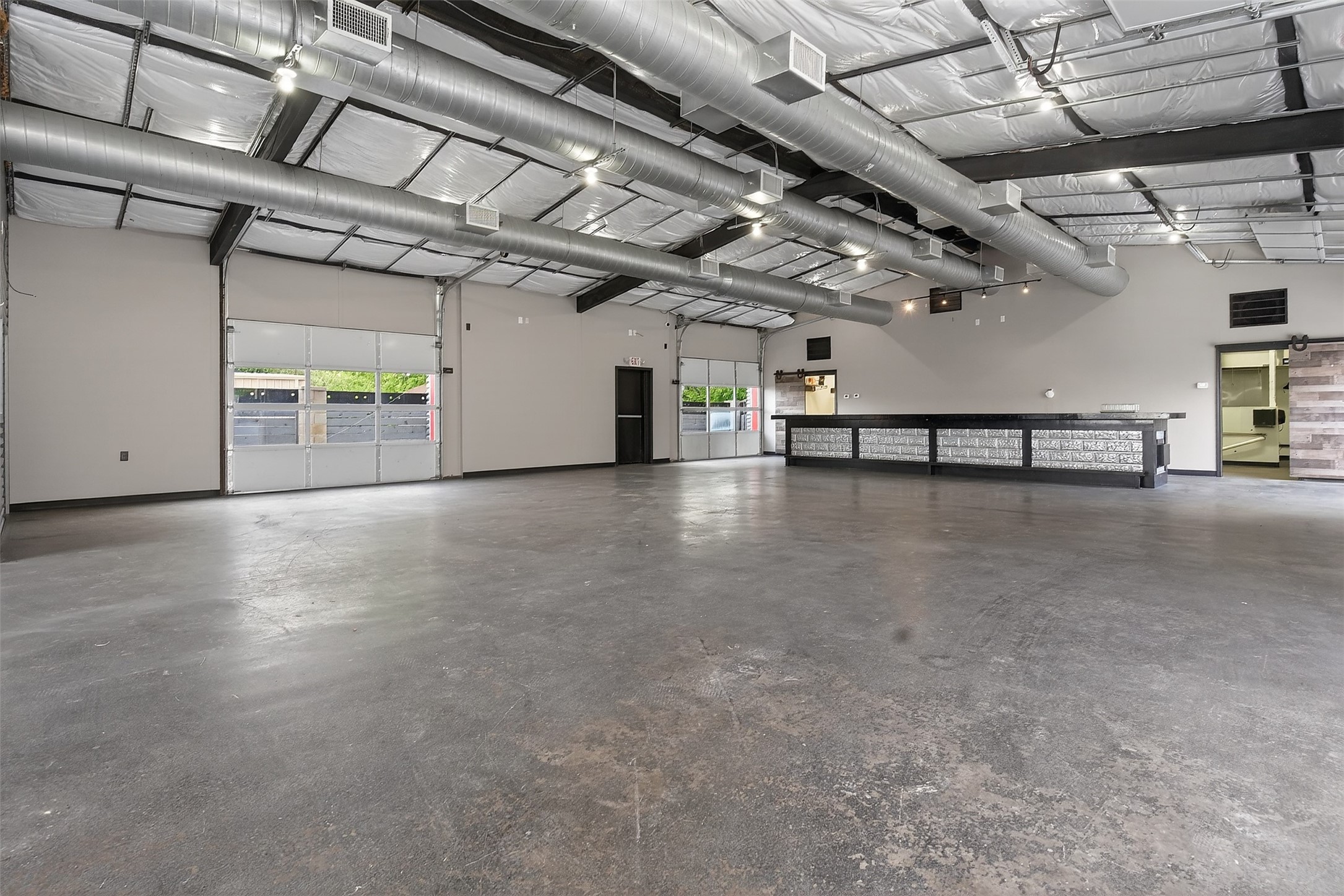 Vacant commercial space with exposed ductwork, two roll-up doors, and a long service counter.