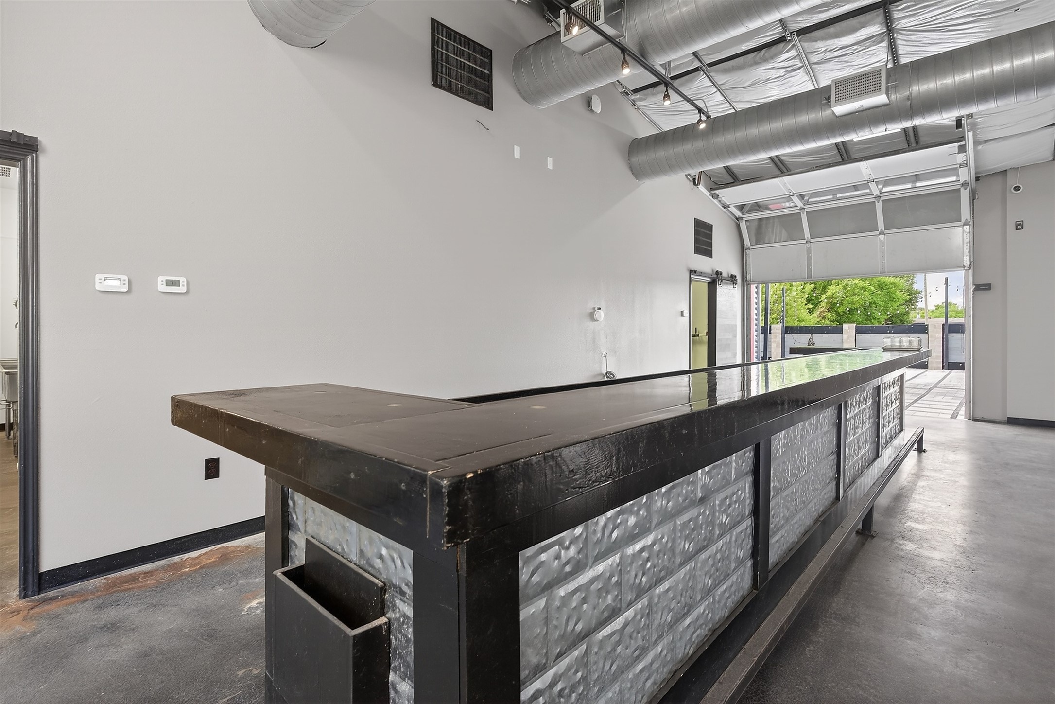 Industrial commercial interior with a long black-and-metal counter and an open garage door.
