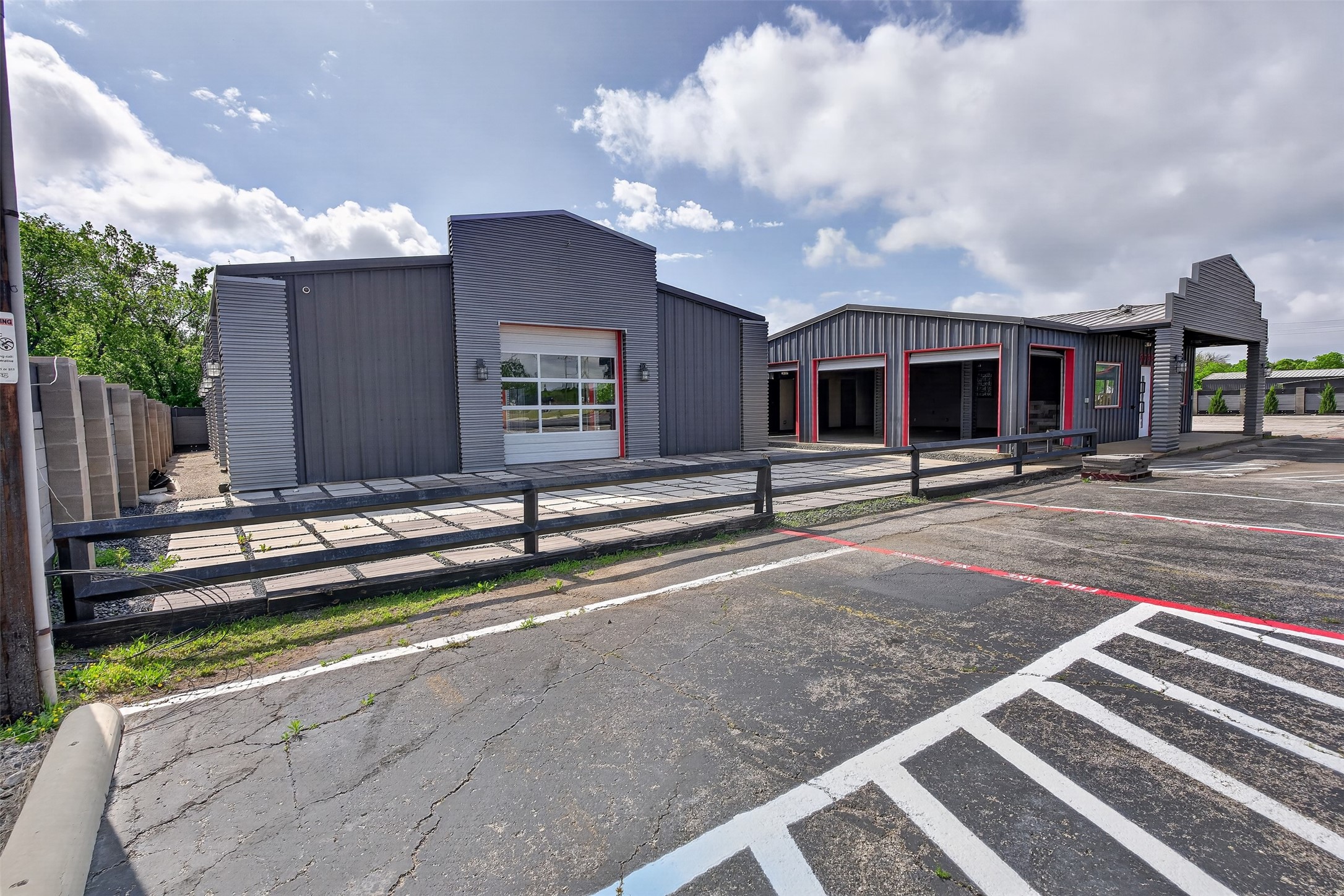 Dark gray commercial building with red-trimmed garage bays beside a marked parking area.