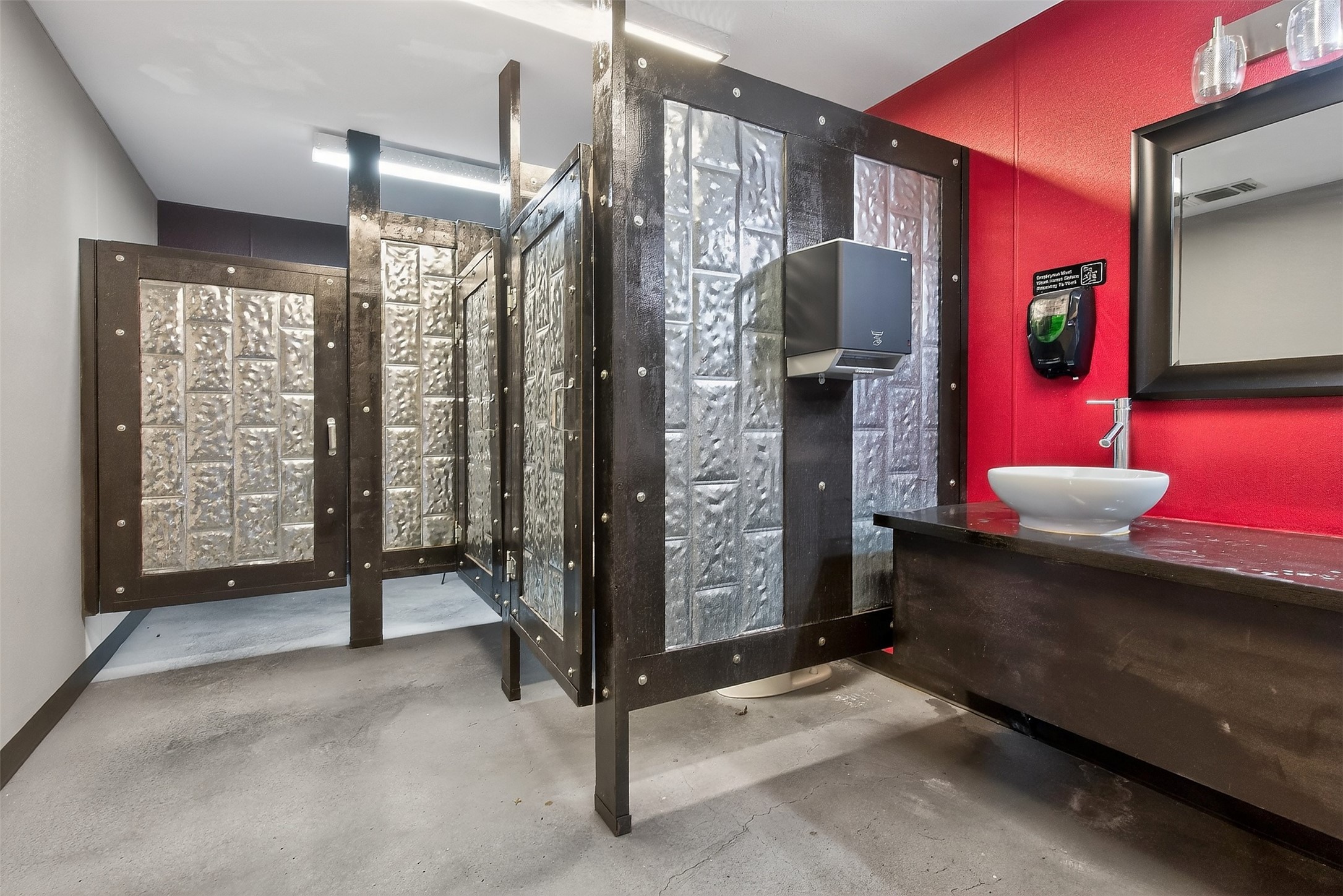 Restroom with textured-glass metal stall partitions, a vessel sink, and a bright red wall.