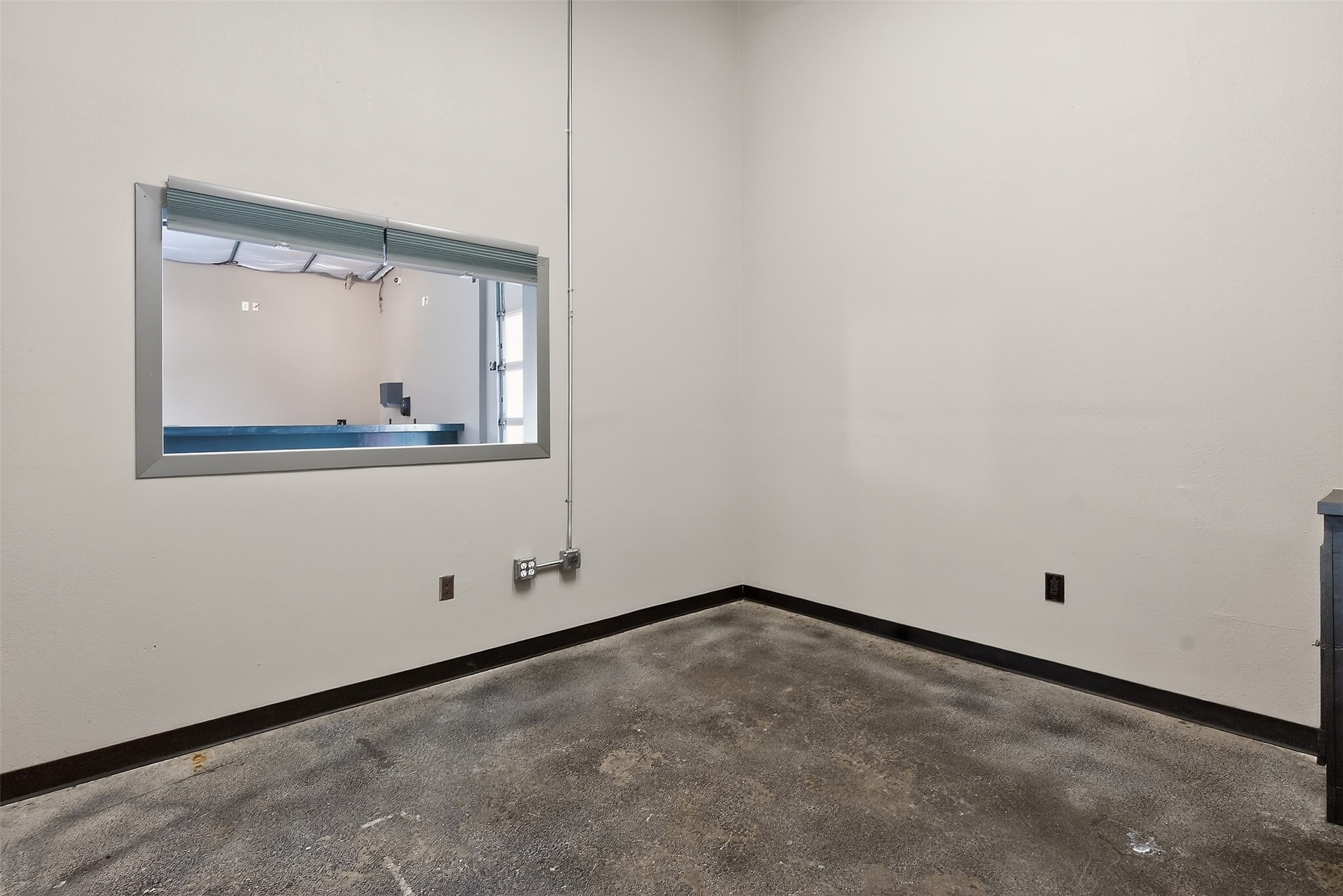 Vacant commercial room with a concrete floor and a large service window in the wall.
