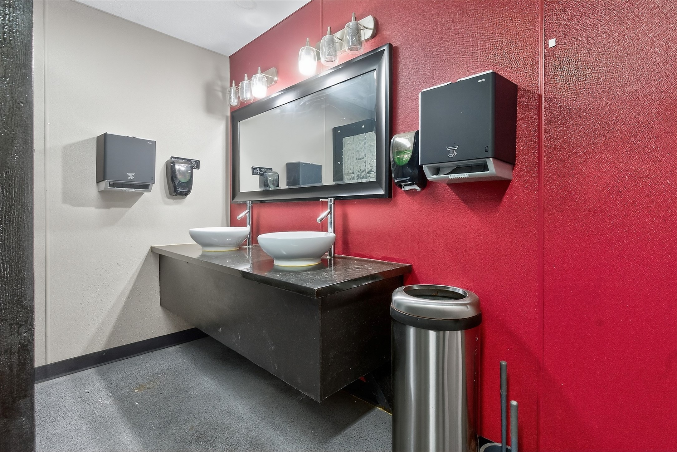 Commercial restroom with two vessel sinks, a large mirror, and a vivid red accent wall.