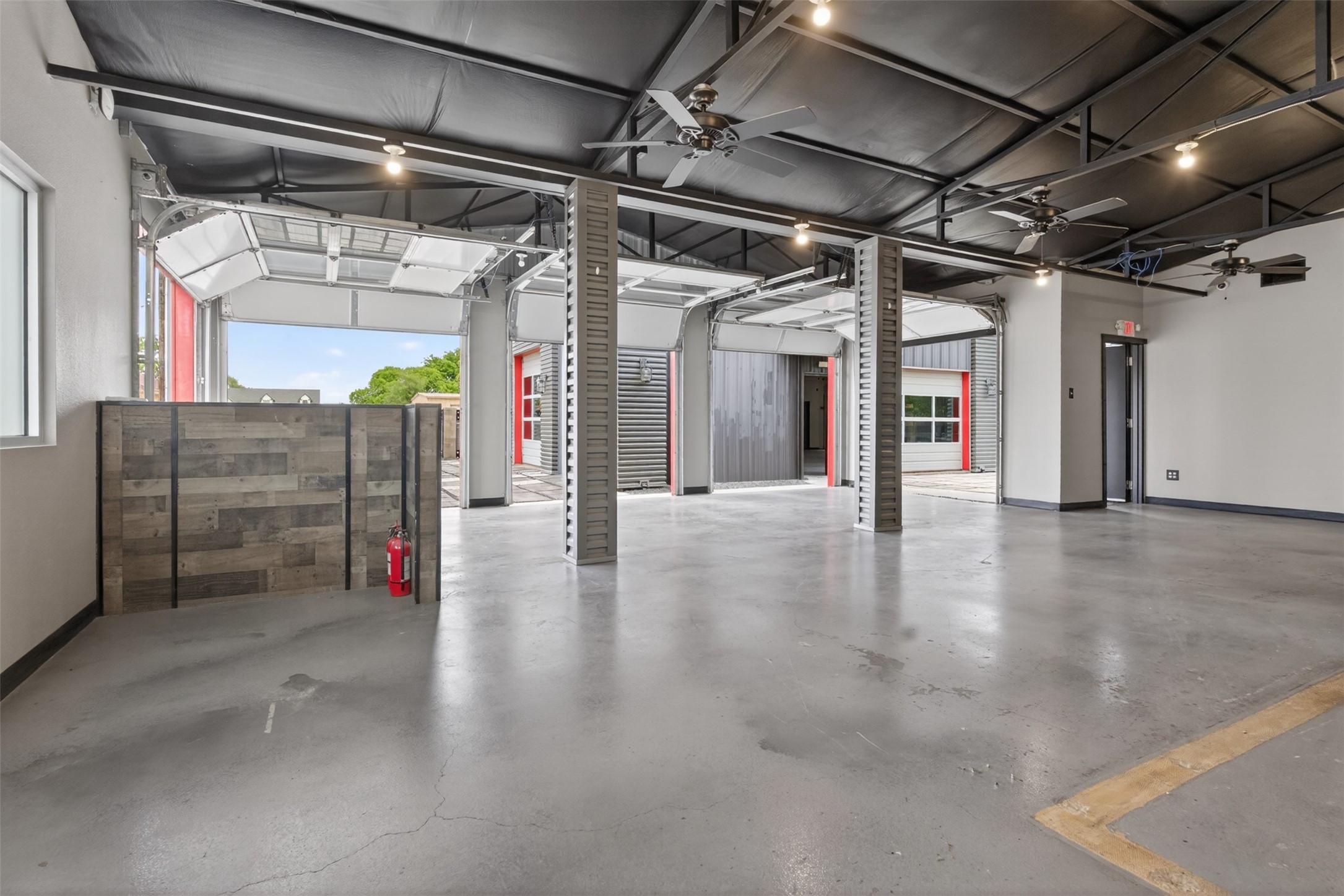 Commercial garage interior with open overhead bay doors, exposed beams, and a concrete floor.