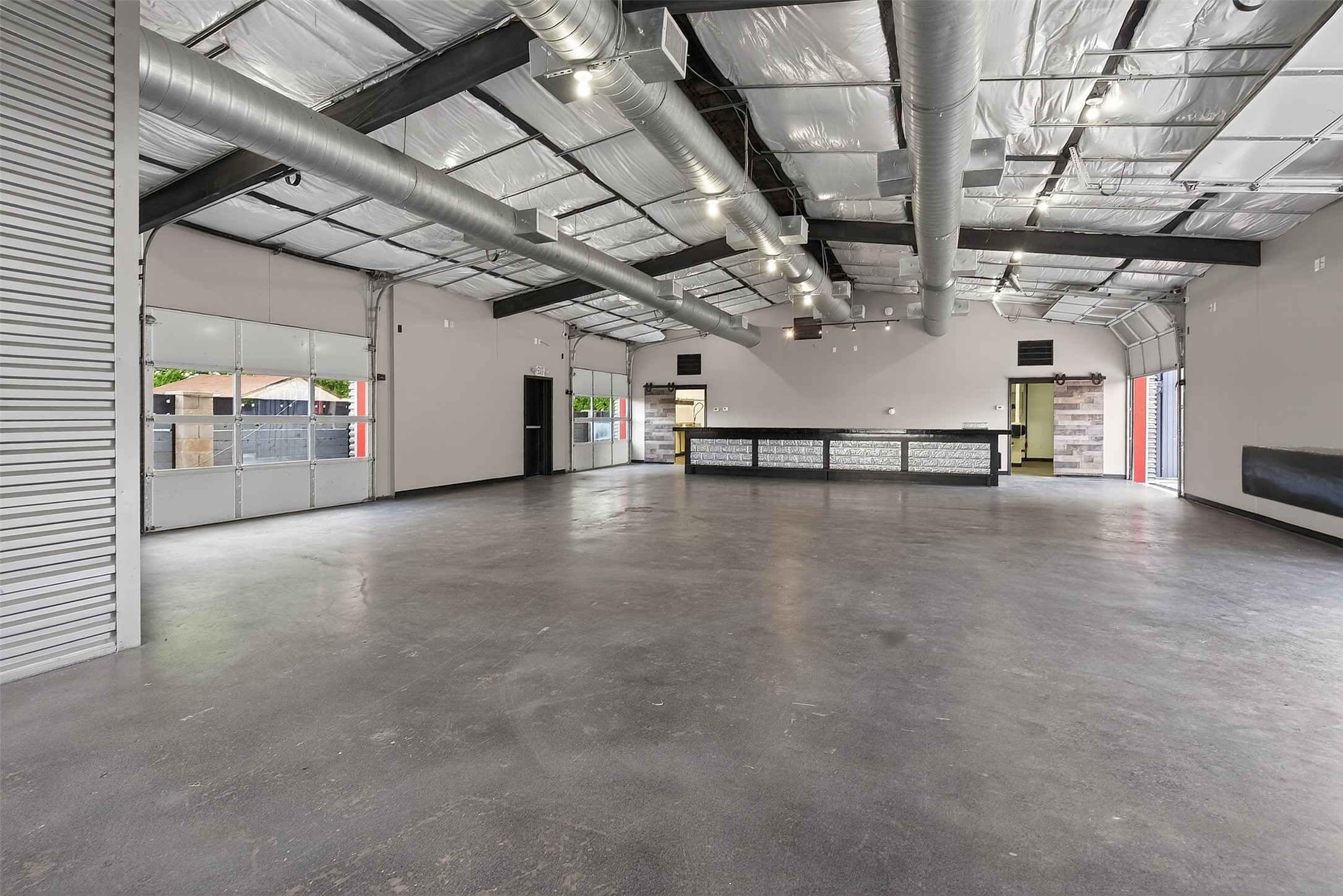 Vacant commercial garage with a broad concrete floor, roll-up doors, exposed ducts, and a long counter.