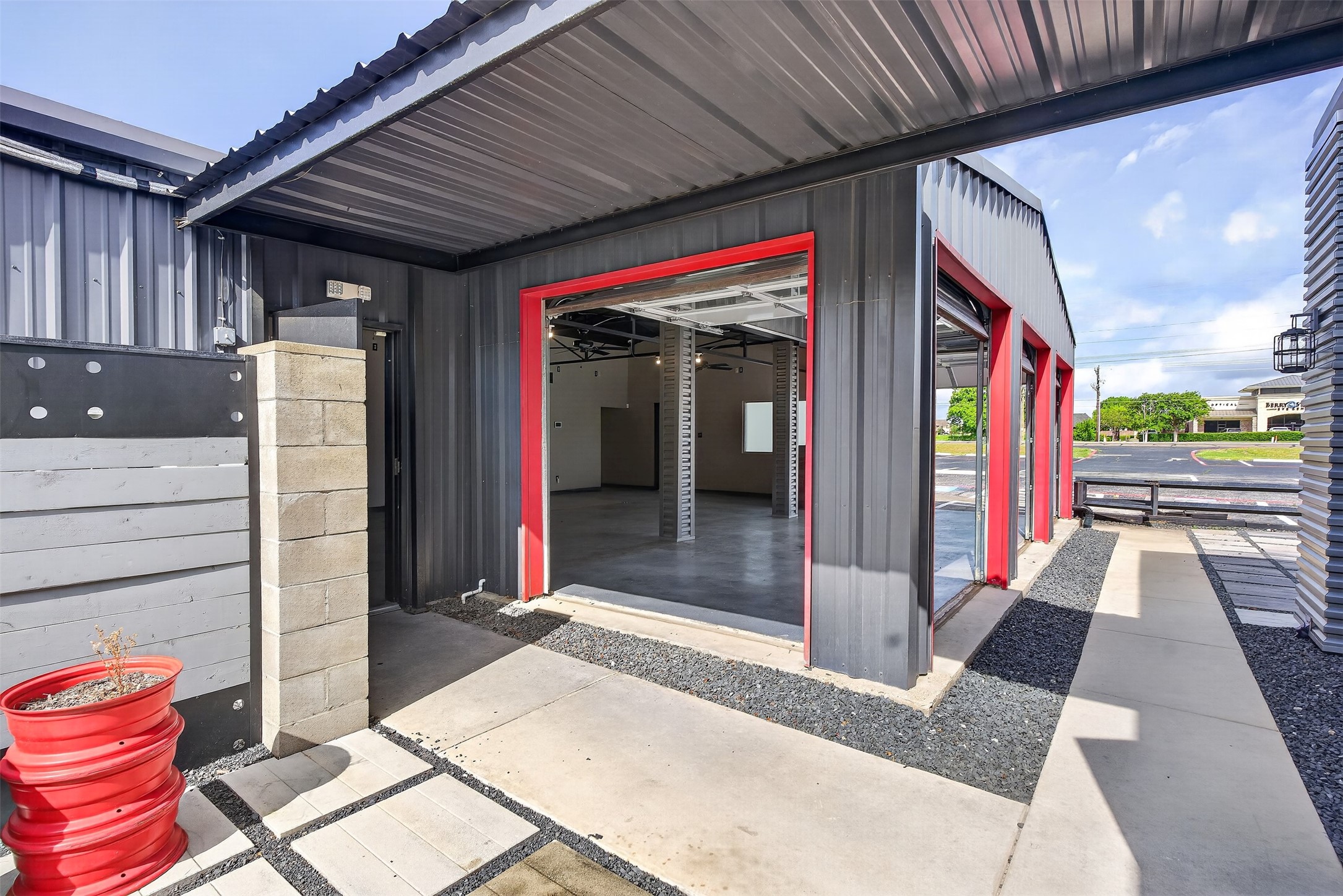 Commercial metal building with open, red-trimmed garage bays and a covered concrete entrance.