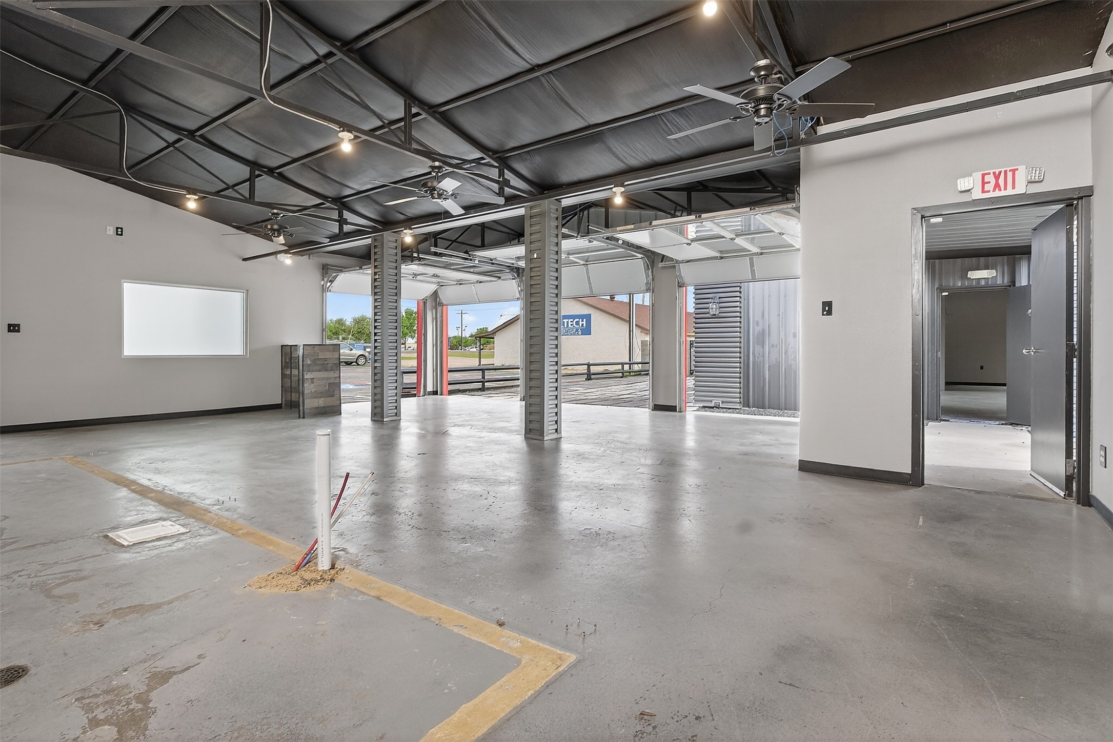Vacant commercial garage interior with open vehicle bays, exposed ceiling beams, and a concrete floor.