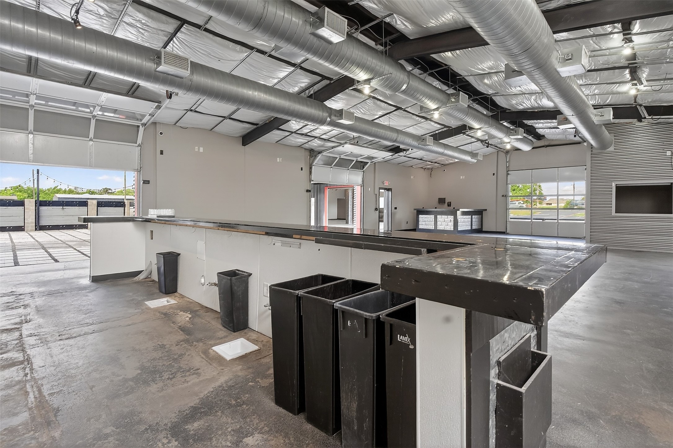 Commercial interior with long work counters, overhead ductwork, and open garage doors.