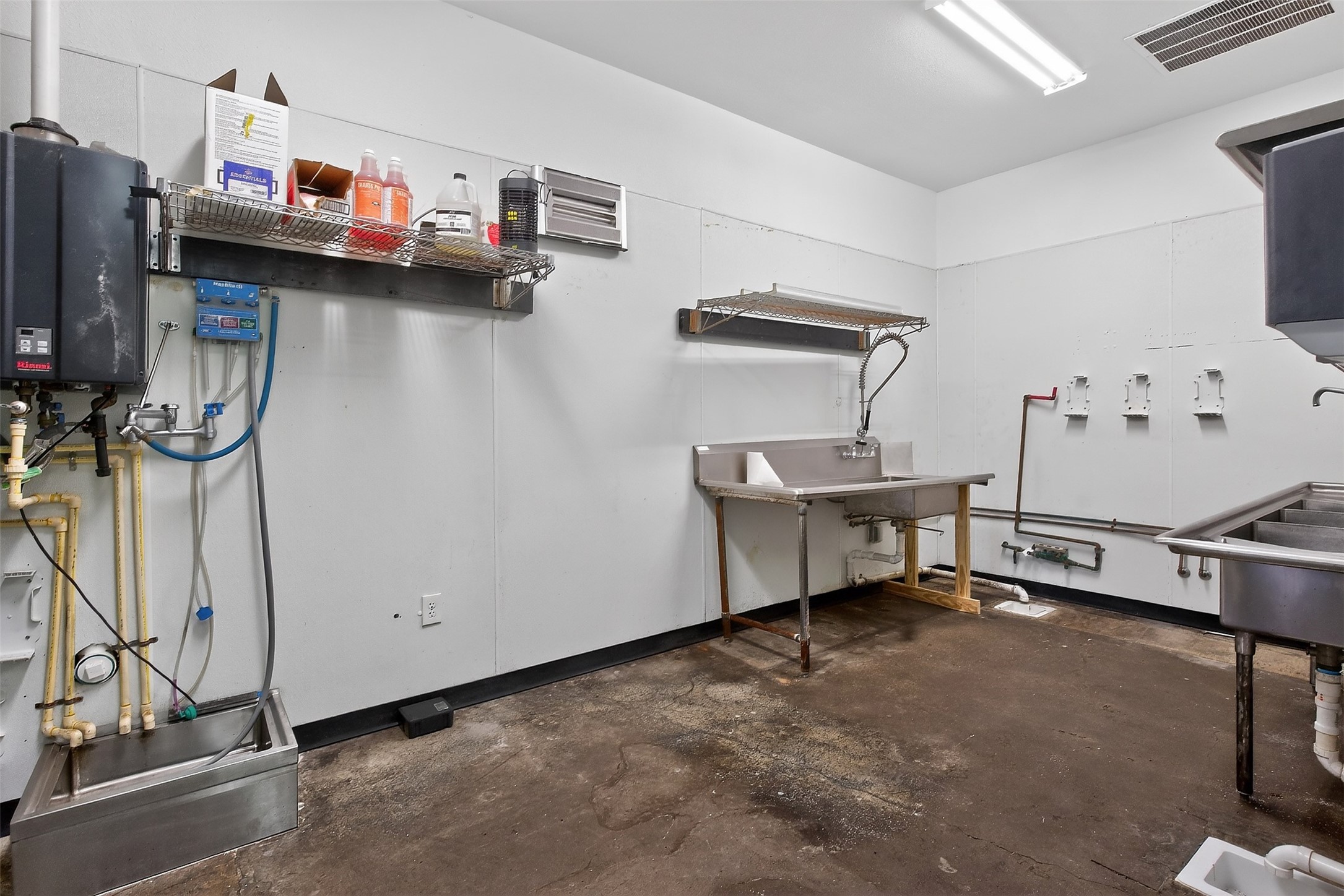 Commercial kitchen wash area with stainless sinks and a wall-mounted pre-rinse spray faucet.