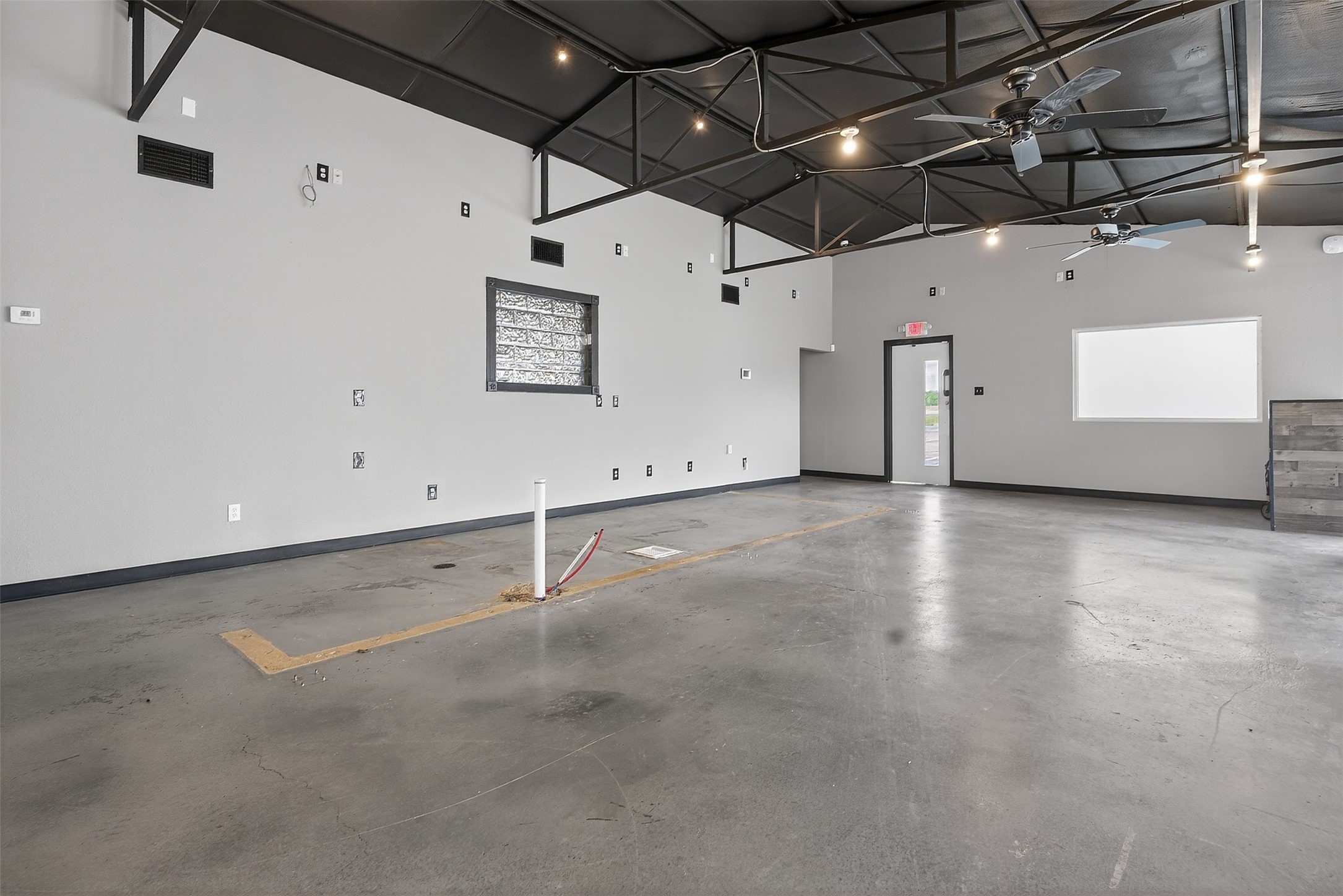 Vacant commercial workshop with an expansive concrete floor, exposed roof trusses, and ceiling fans.