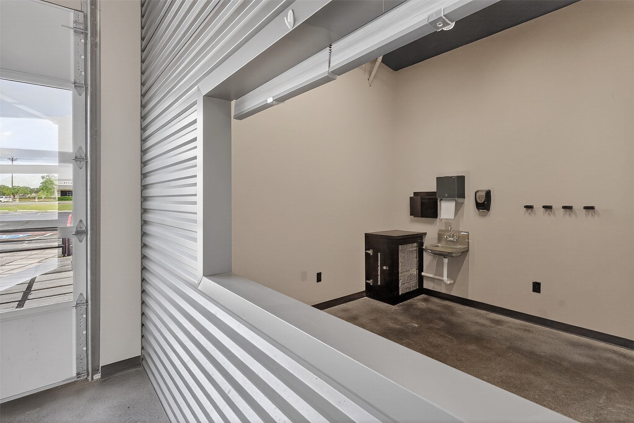 Commercial interior with a partially open garage door, corrugated metal partition, and wall-mounted sink.