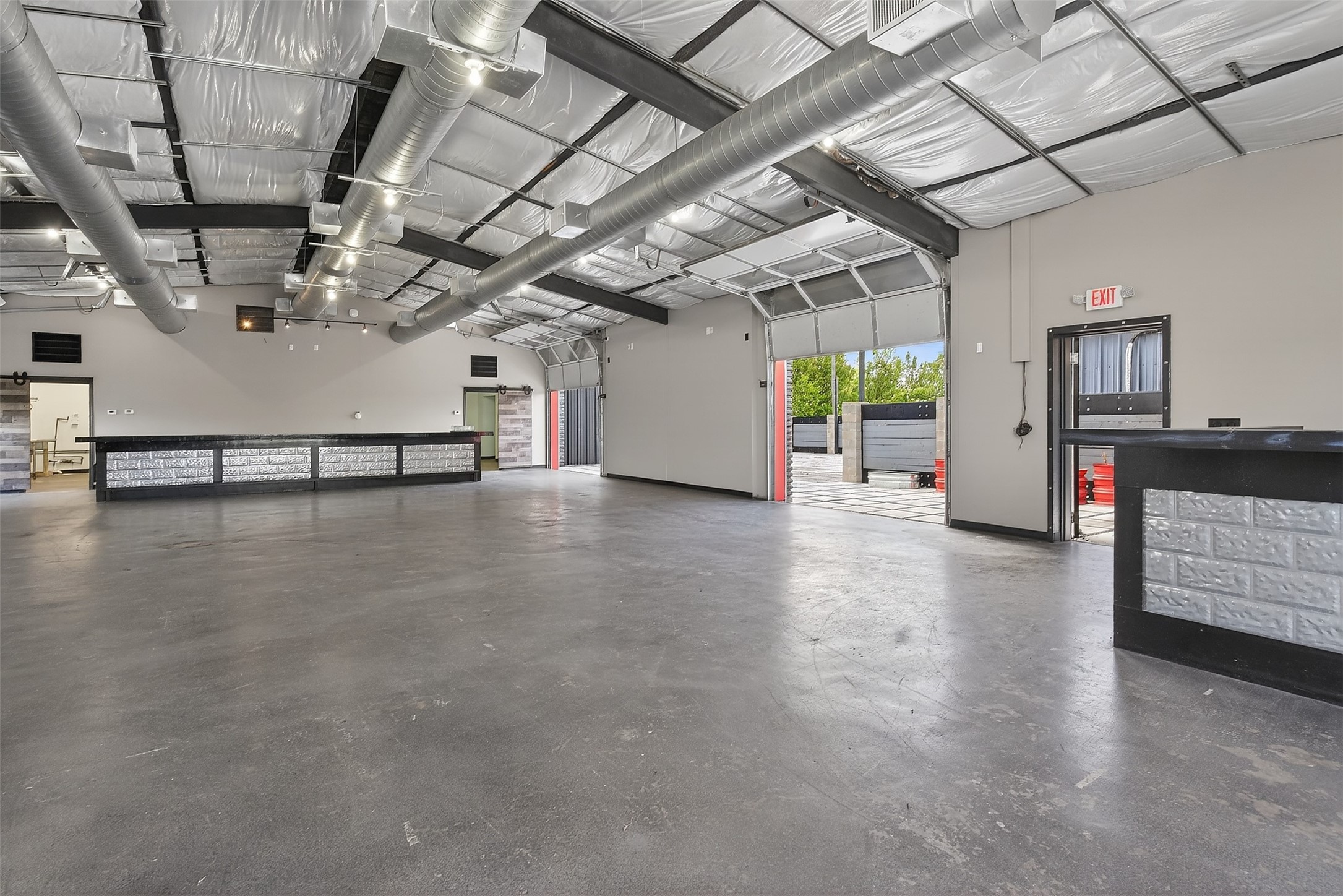 Vacant commercial garage interior with concrete floor, service counters, and open roll-up doors.
