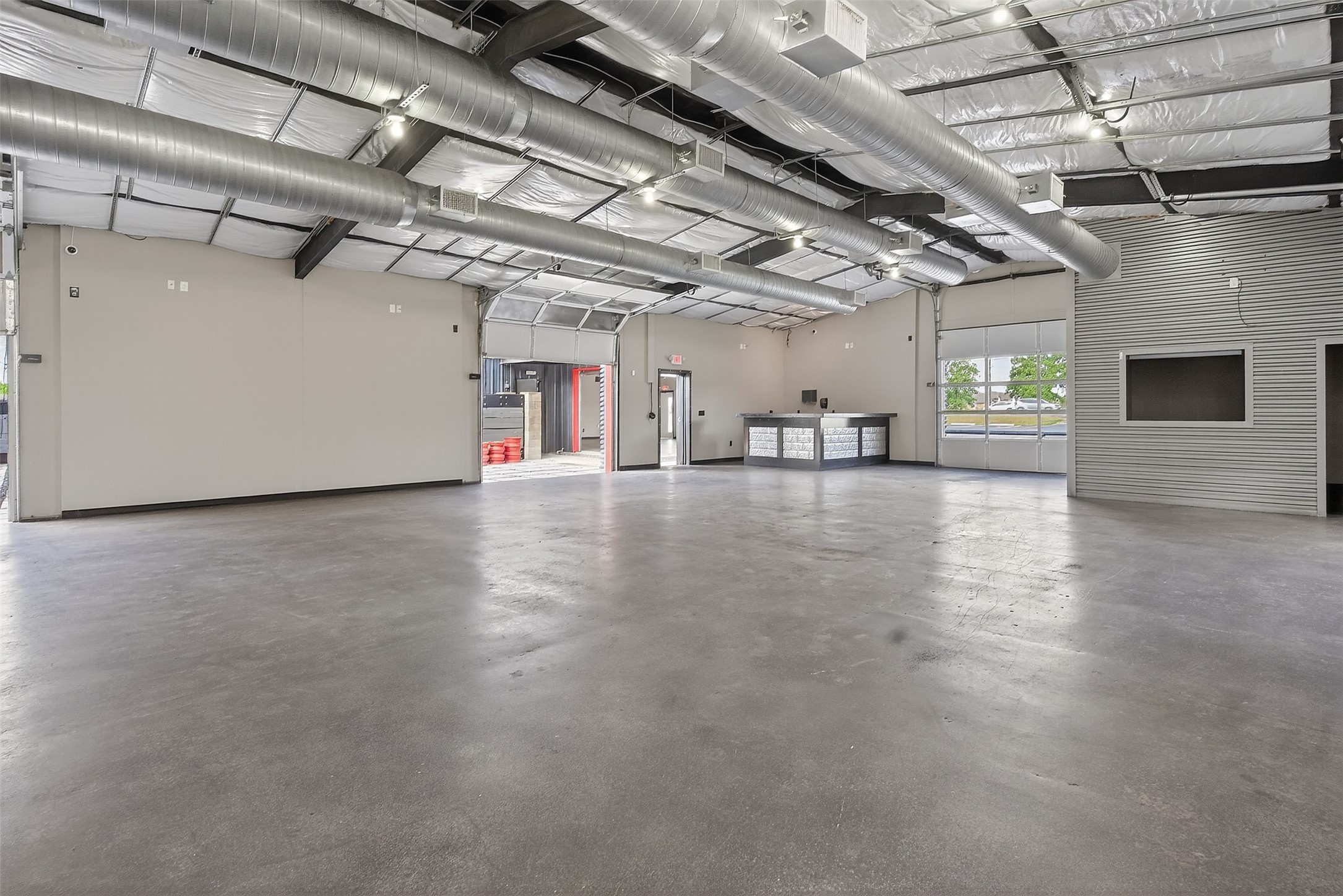 Vacant commercial interior with concrete floors, exposed ductwork, a service counter, and large garage doors.