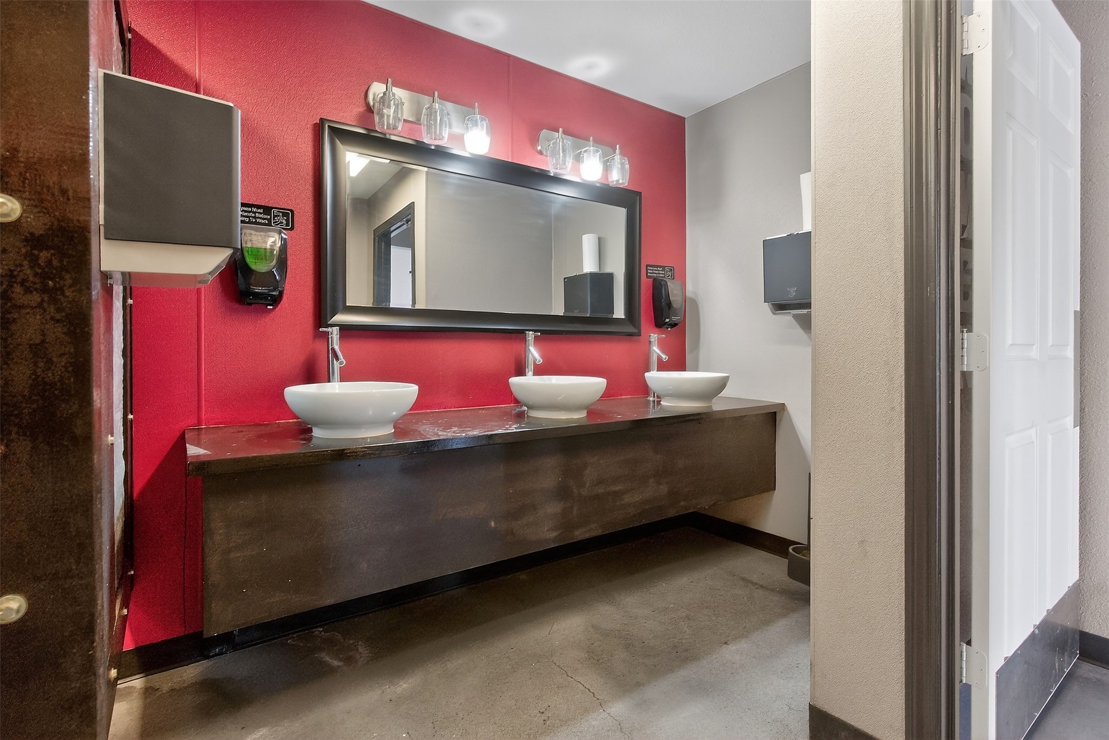 Commercial bathroom with three vessel sinks, a long dark vanity, and a vivid red accent wall.