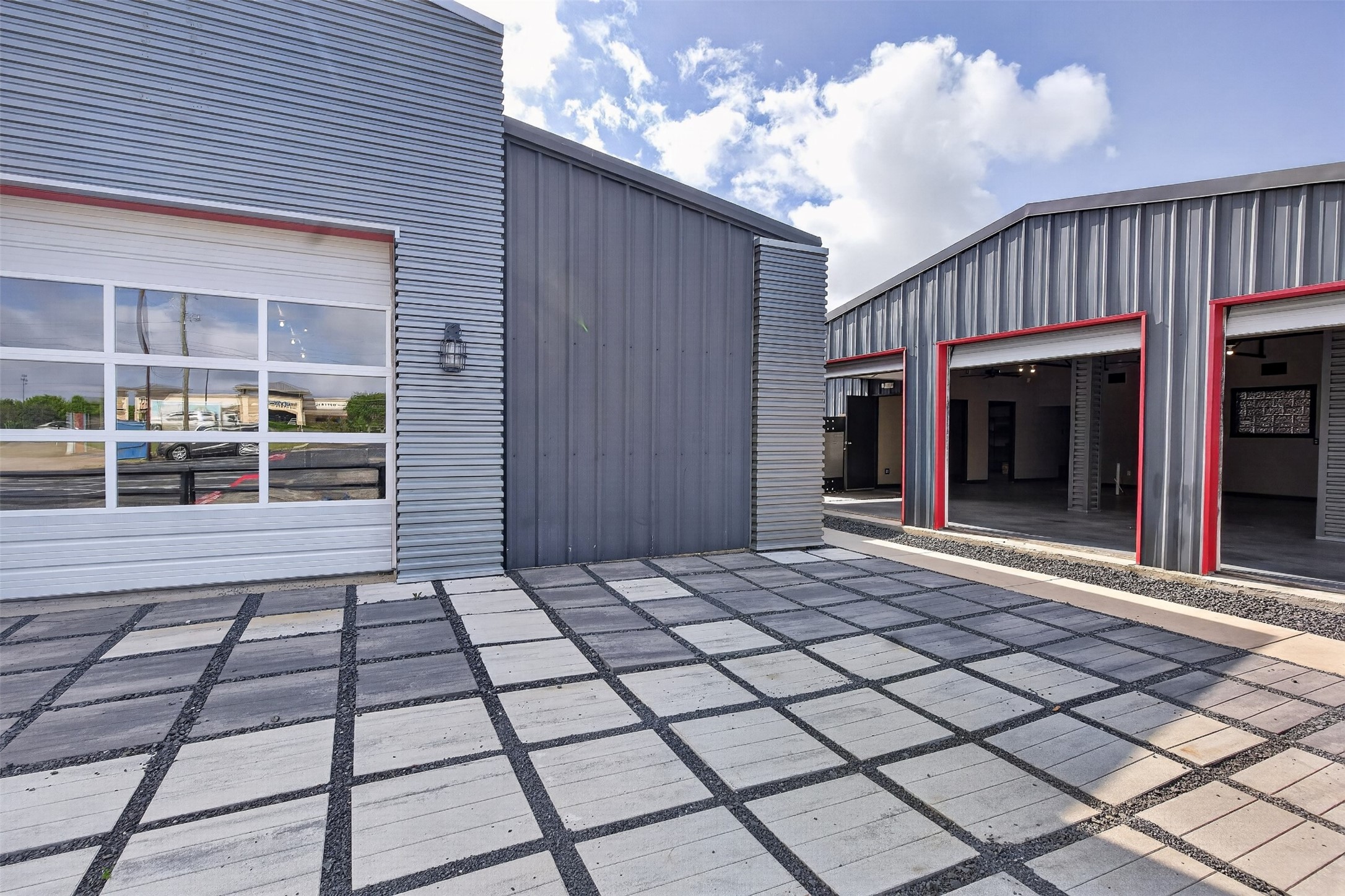 Modern metal commercial building with red-trimmed open garage bays and a paved courtyard.