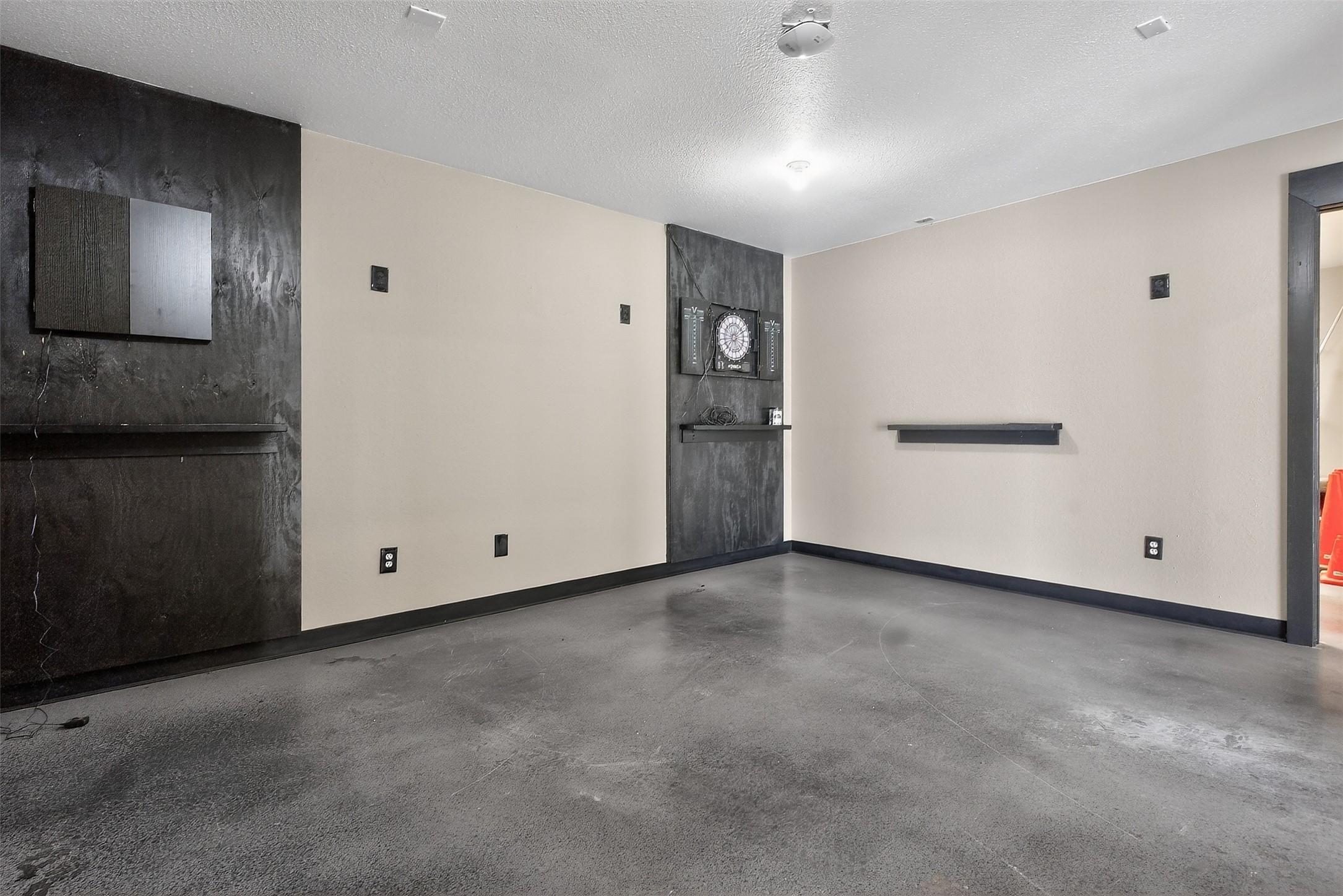 Empty room with a concrete floor, dark accent panels, and a dartboard on the back wall.
