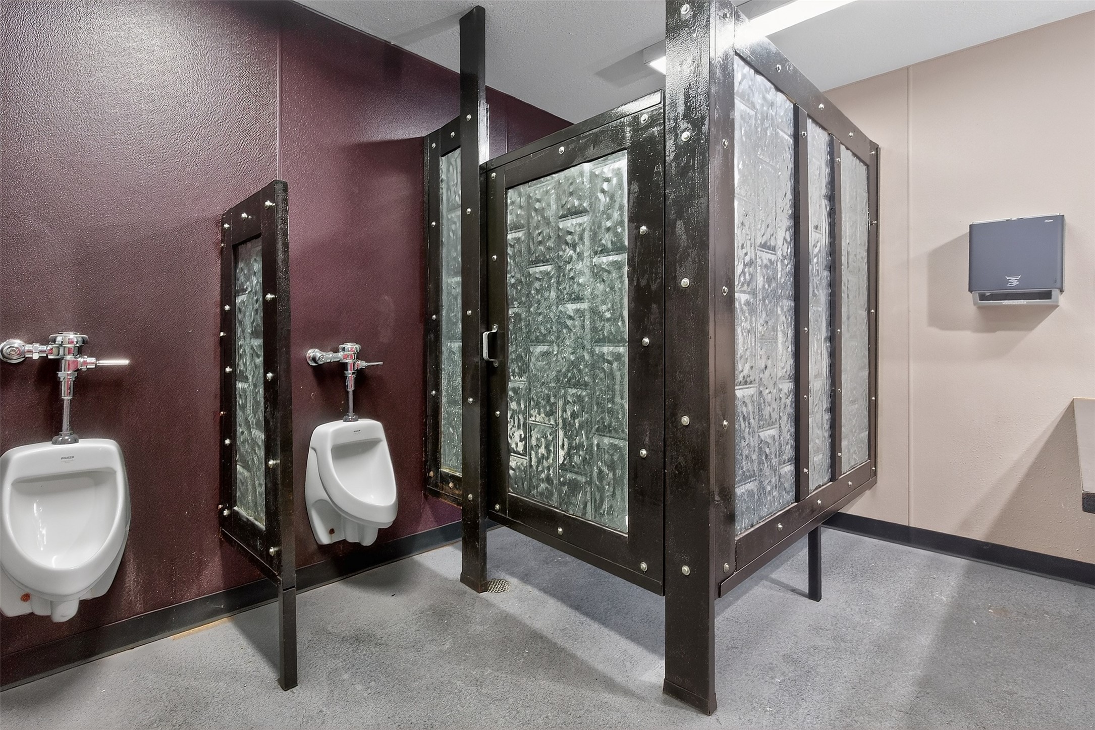 Commercial restroom with white urinals and dark metal privacy partitions with translucent panels.