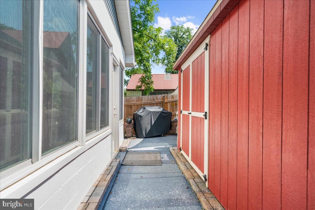 Side patio walkway between the house and red shed, with a covered grill at the end.