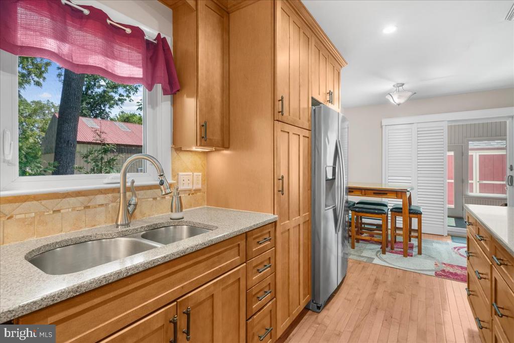 Kitchen with honey-toned cabinets, granite counters, a double sink, and a small dining area with stools.