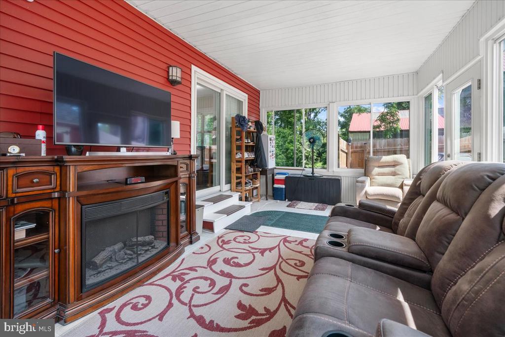 Furnished sunroom with a red accent wall, wraparound windows, and a brown reclining sectional.