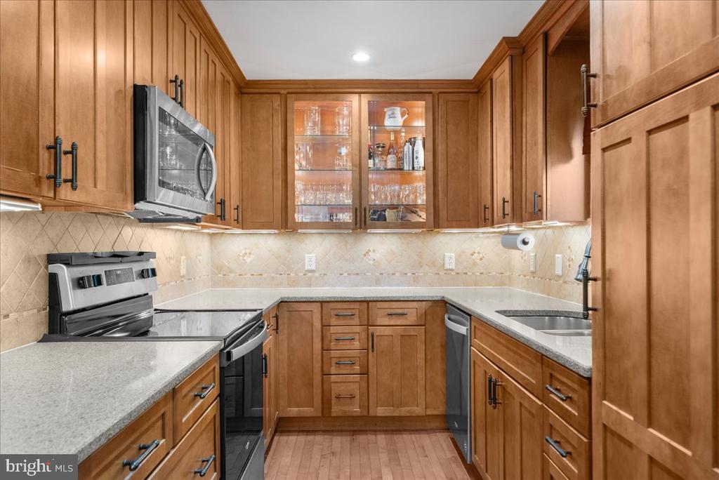 U-shaped kitchen with warm wood cabinetry, stone countertops, and stainless-steel appliances.