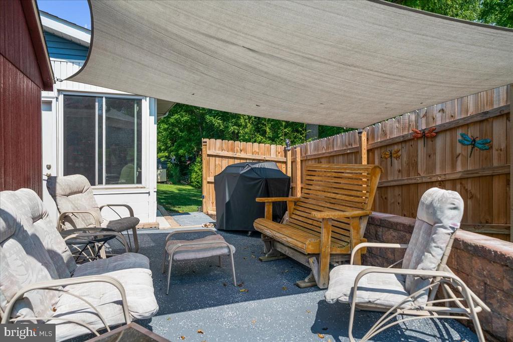 Patio with cushioned chairs, a wooden bench, a covered grill, and a large shade canopy.
