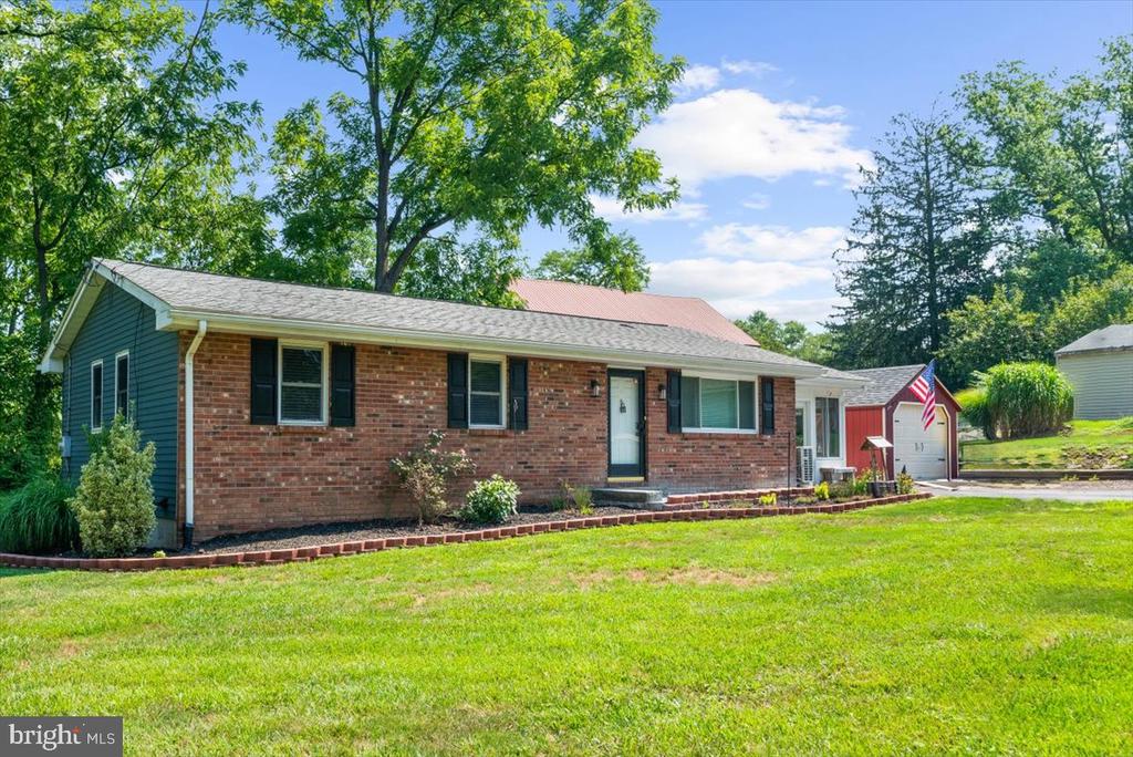 Single-story brick house with dark shutters, a red garage, and a broad front lawn.
