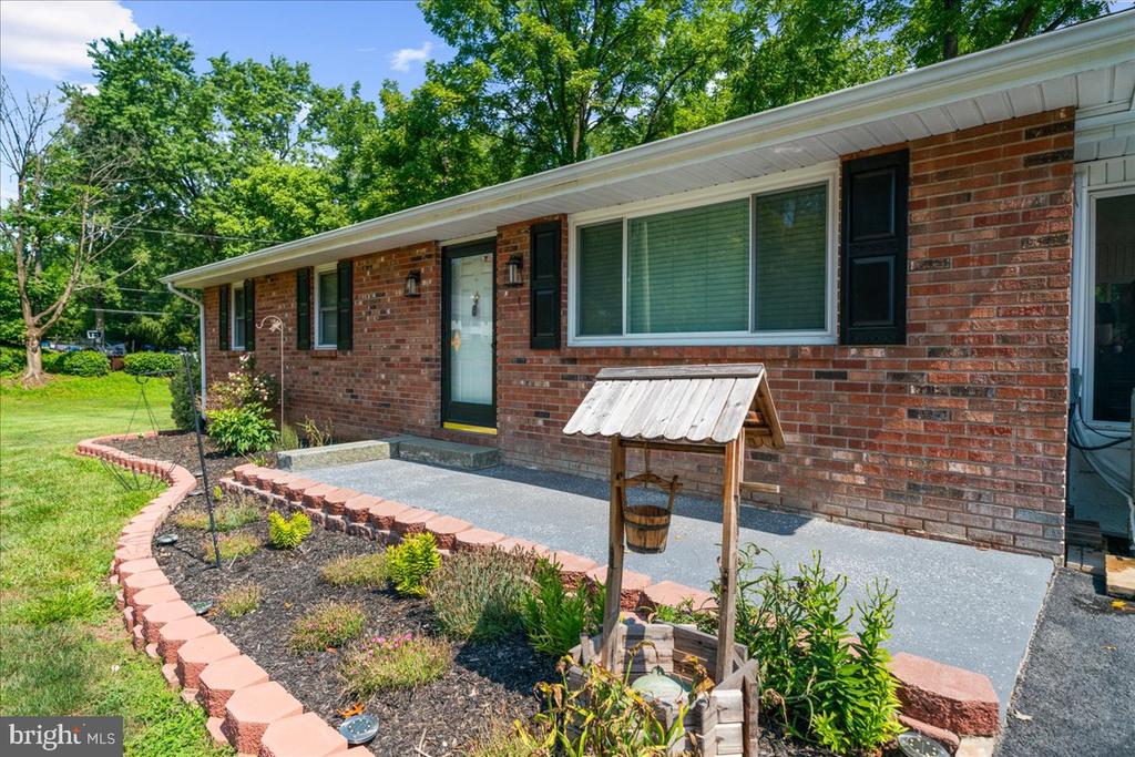 Single-story brick home with dark shutters, a broad concrete walkway, and a curved garden bed.