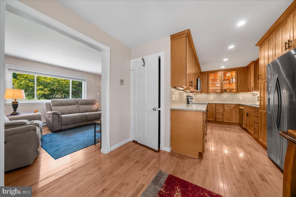 Kitchen with warm wood cabinets and stainless appliances opening to a living room with gray sofas and a blue rug.